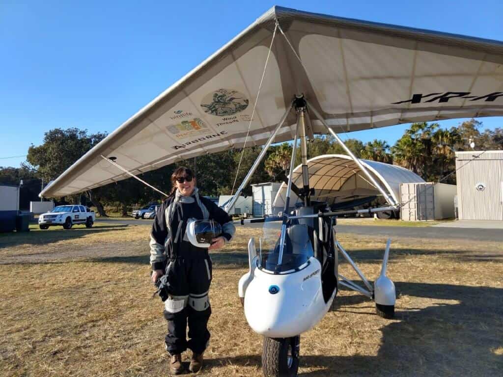 Amellia Formby standing next to her white microlight aircraft in a flying suit at Lake Macquarie airport
